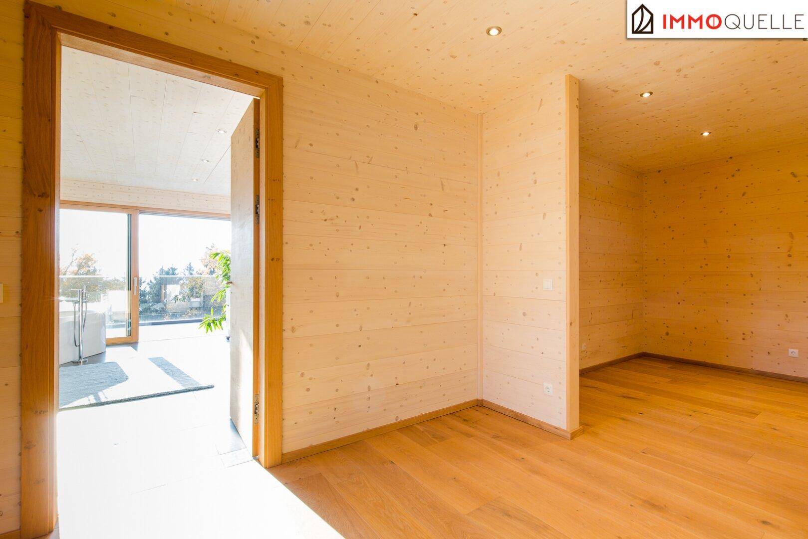 Heller Raum mit Holzboden und Holzwänden, offen zu einem weiteren Bereich, ideal für individuelle Gestaltung.