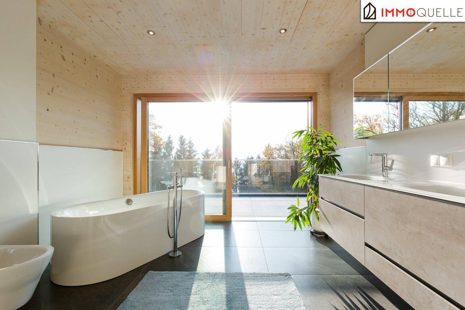 Helles Badezimmer mit freistehender Badewanne, Doppelwaschbecken und großen Fenstern mit viel Sonne.