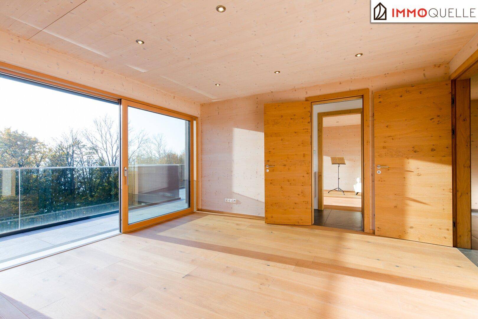 Helles Schlafzimmer mit Holzboden und großen Schiebetüren zum Balkon mit Aussicht.