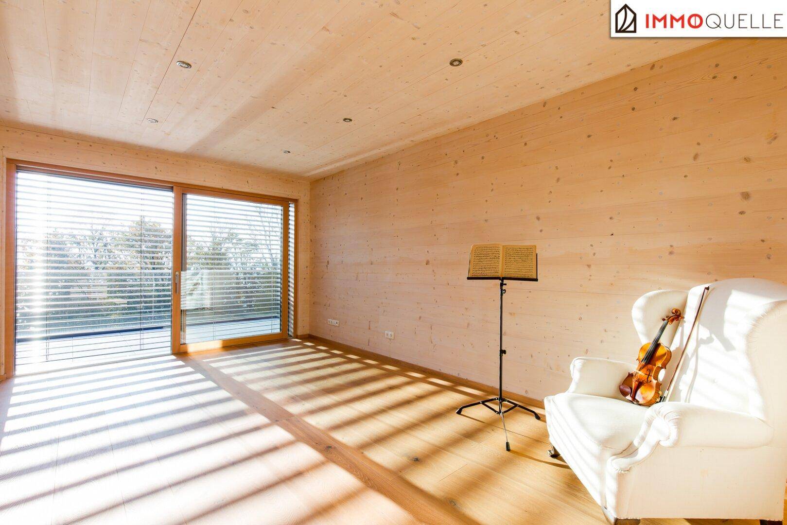 Heller Raum mit Holzboden, großen Fenstern und einem Notenständer, ideal als Arbeits- oder Musikzimmer.