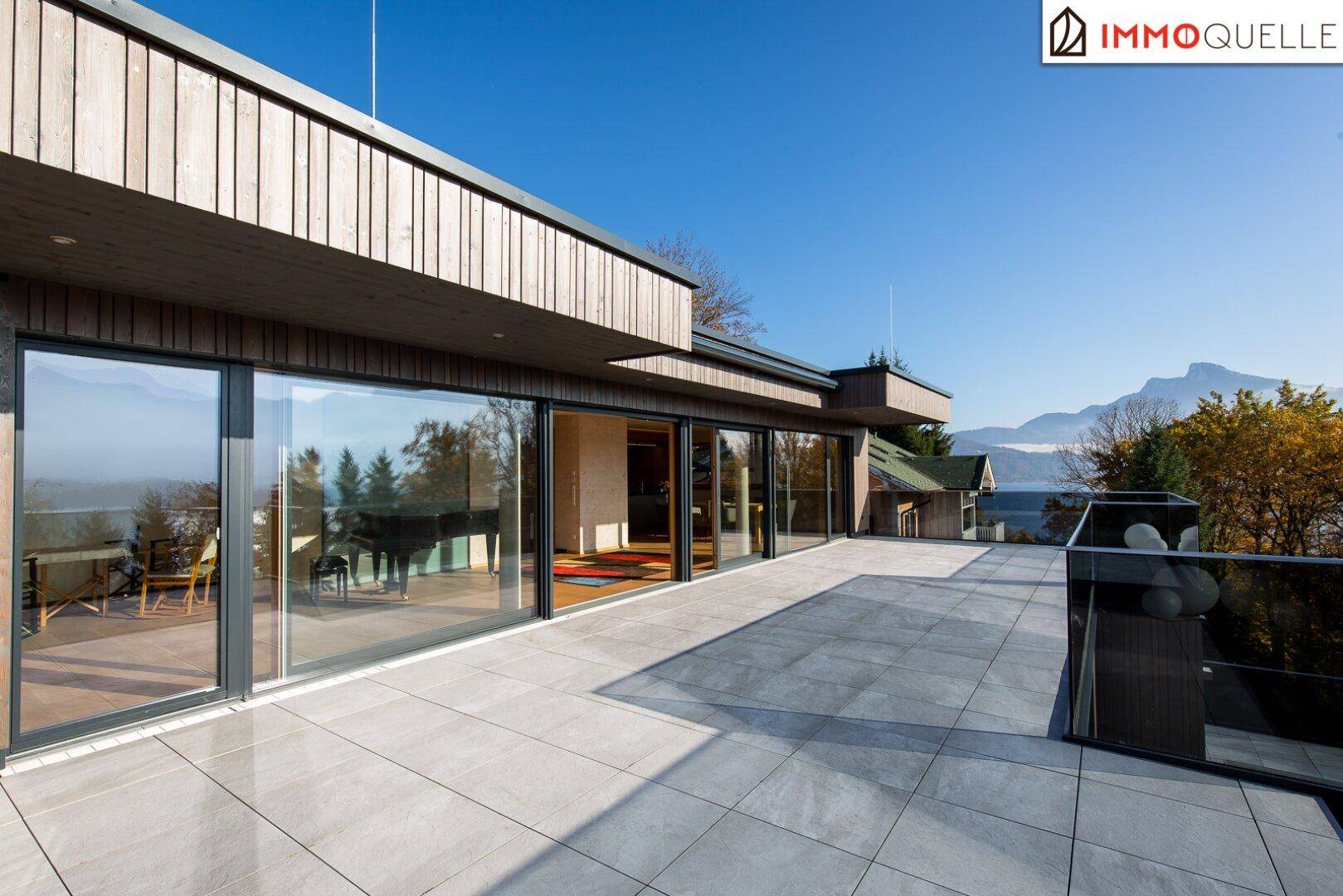 Weitläufige Terrasse mit moderner Architektur, Glasgeländer und Panoramablick auf See und Berge.