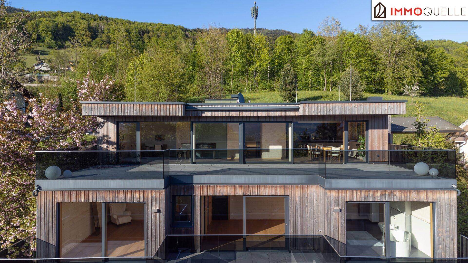 Moderne Architektur mit Holzfassade, großen Glasflächen und Terrassen in grüner Umgebung.