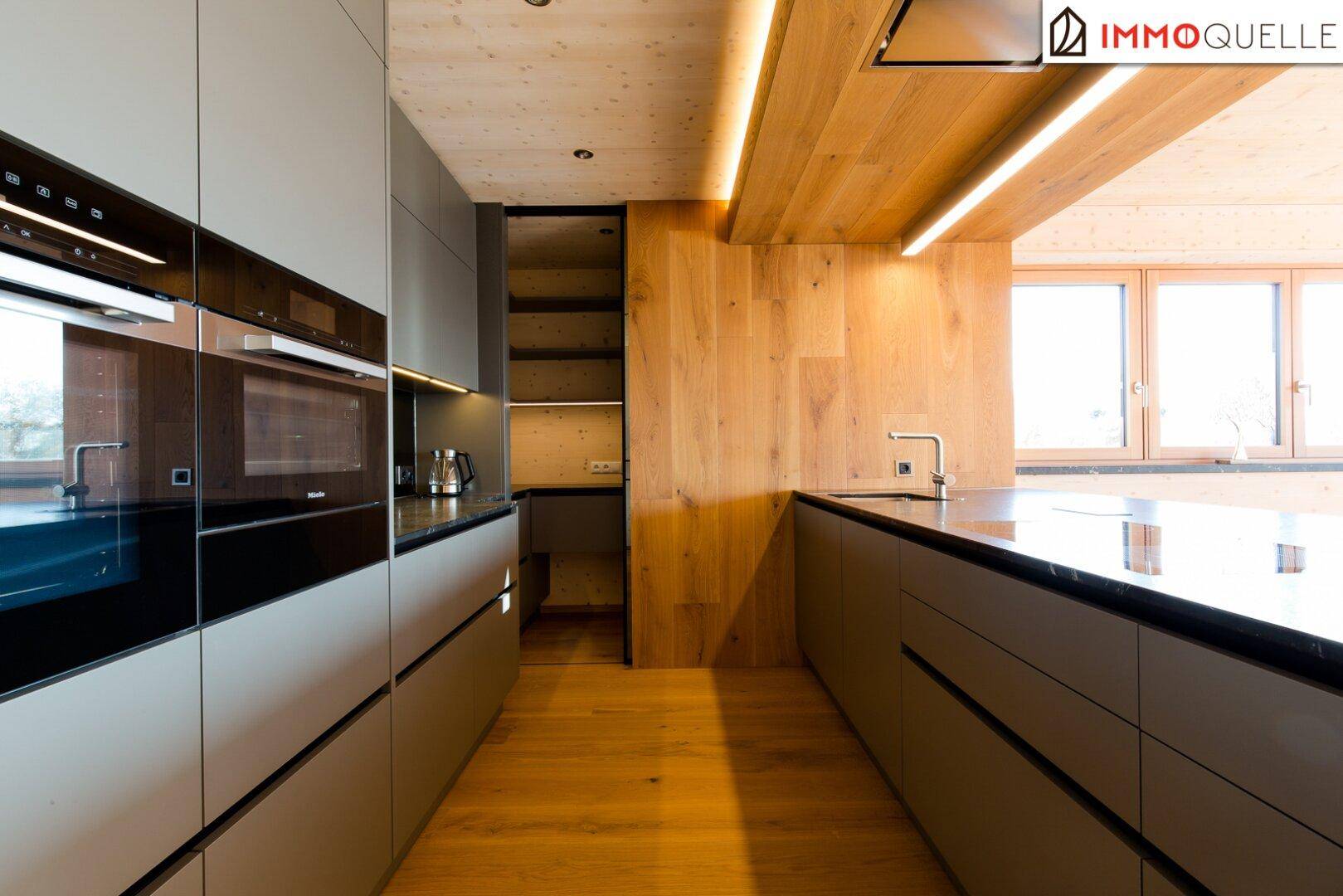 Moderne Küche mit dunklen Fronten, Holzdecke und integrierten Geräten sowie einer Speisekammer.