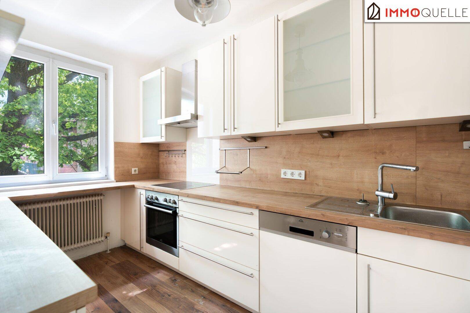 Moderne Einbauküche mit weißen Schränken, Holz-Arbeitsplatten und Fenster mit Blick ins Grüne.
