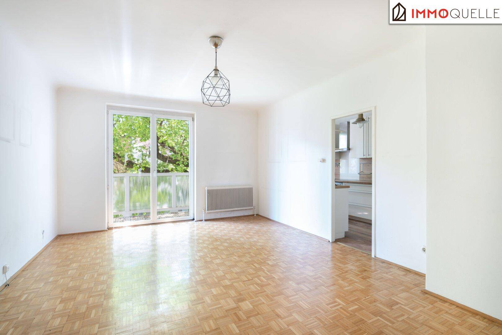 Heller, leerer Wohn-Essbereich mit Fischgrätparkett und direktem Zugang zum sonnigen Balkon.