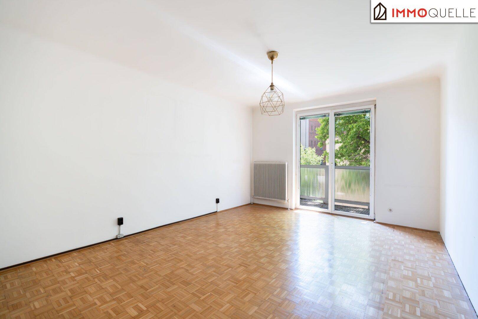 Helles, leeres Schlafzimmer mit Parkettboden und großem Fenster mit Balkonzugang.