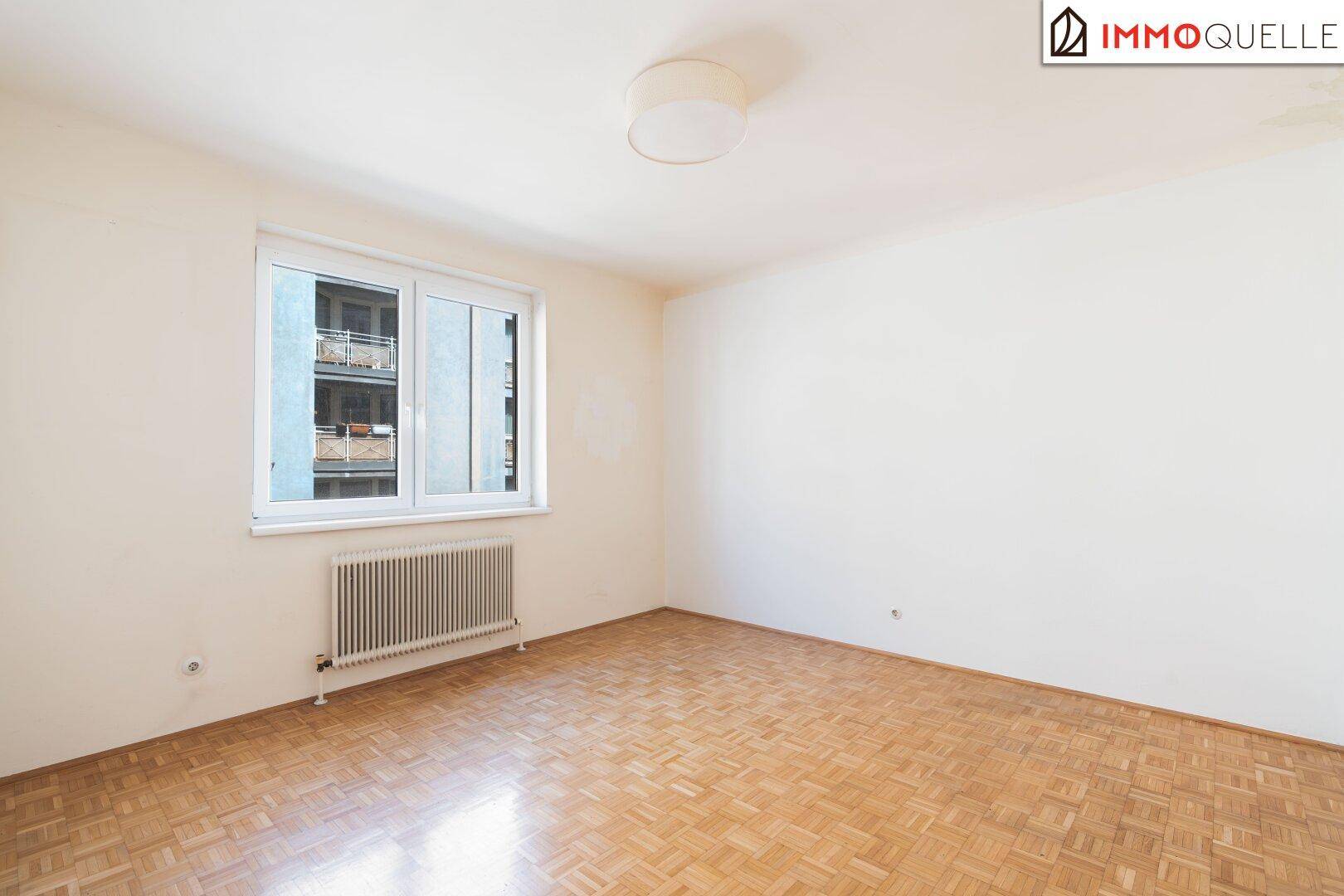 Unmöbliertes Schlafzimmer mit Parkettboden und einem großen Fenster für ausreichend Tageslicht.