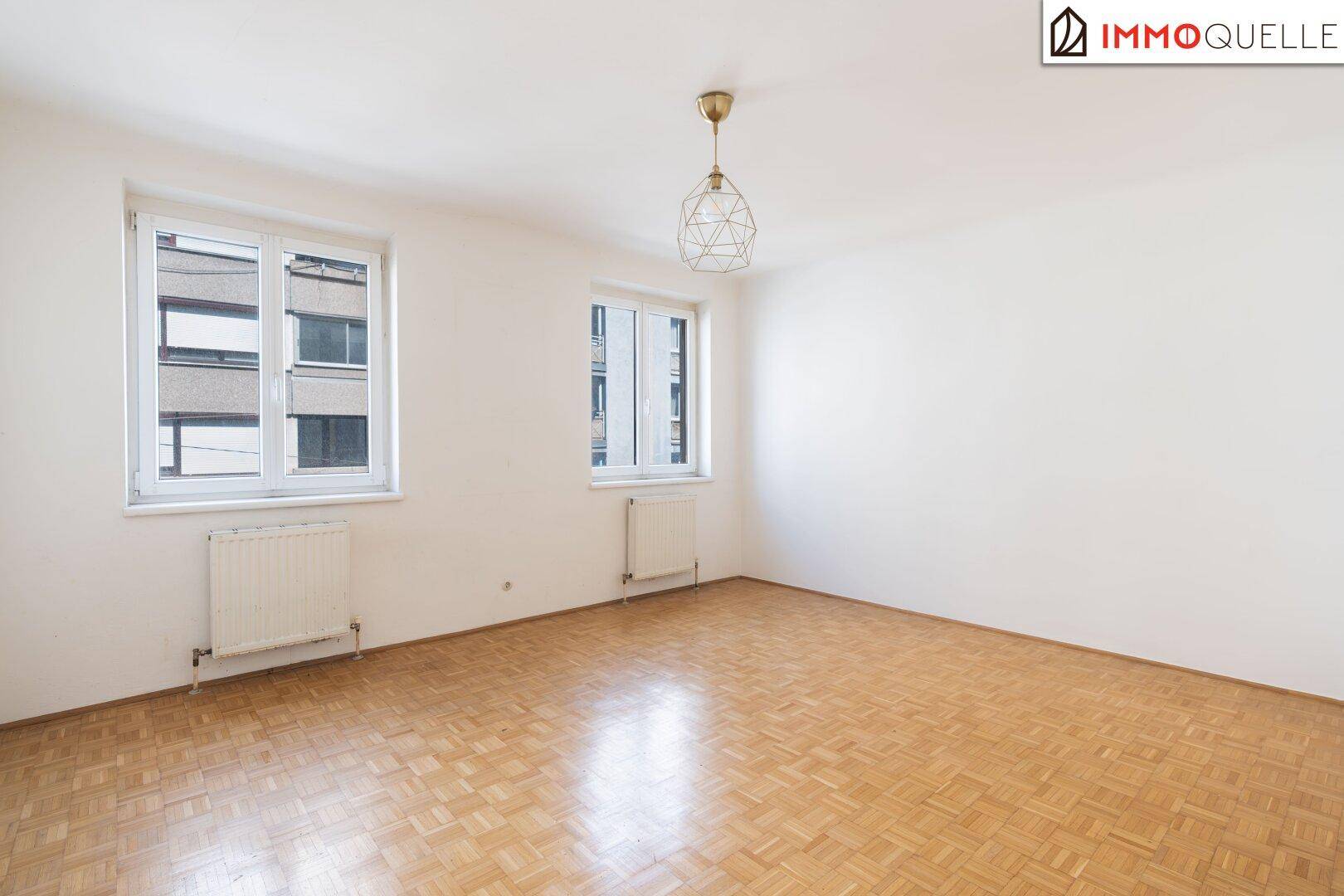 Geräumiges, unmöbliertes Schlafzimmer mit Parkettboden und zwei hellen Fenstern.
