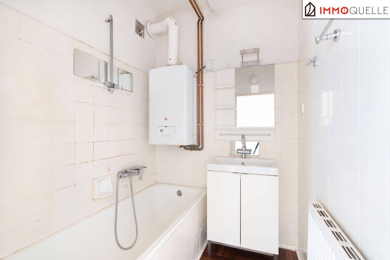 Funktionales Badezimmer mit Badewanne, Einzelwaschbecken und Wandfliesen in hellem Ton.