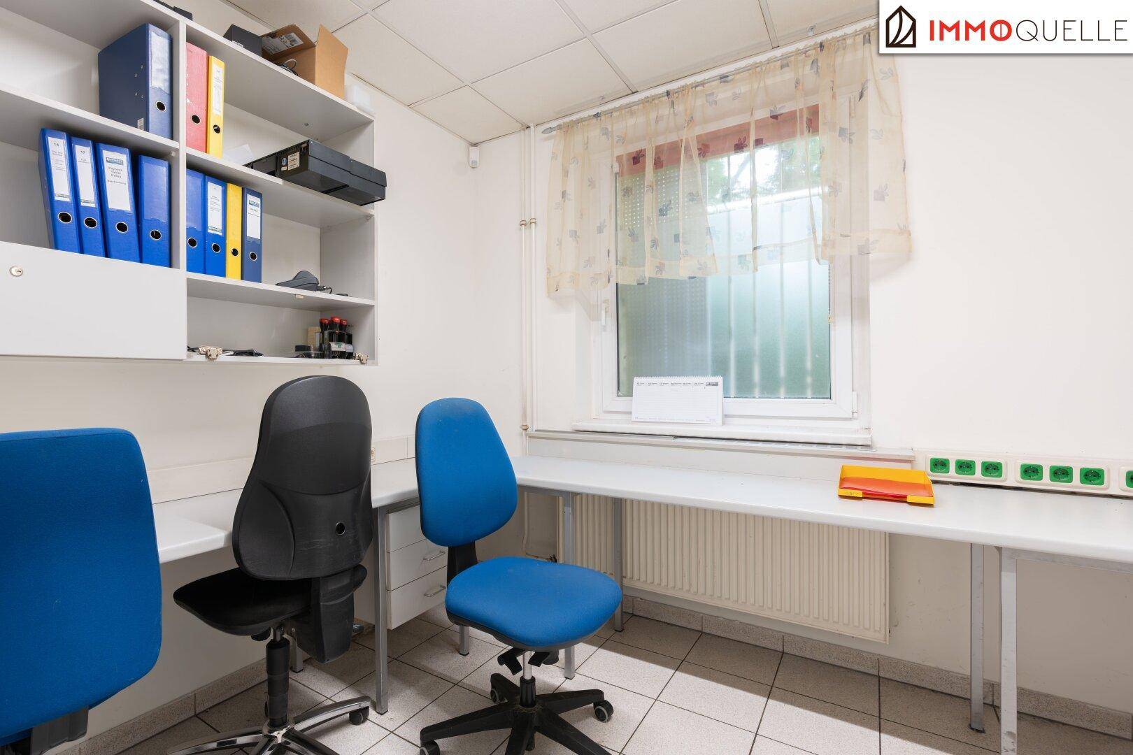 Helles Büro mit Schreibtischen, Bürostühlen und einem Fenster, das für natürliches Licht sorgt.