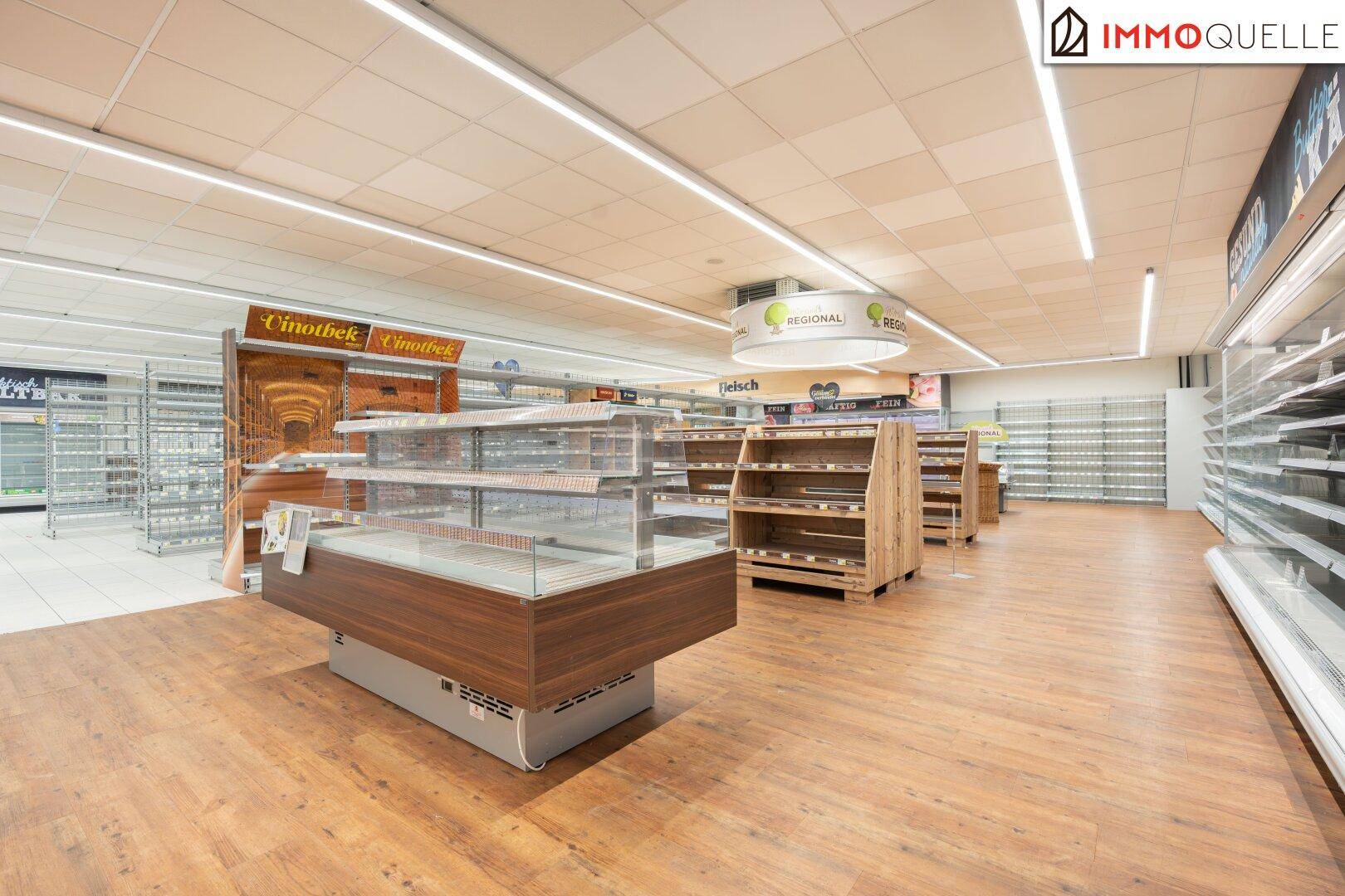 Gangbereich eines Supermarktes mit leeren Regalen und Holzböden, bereit für neue Warenbestückung.