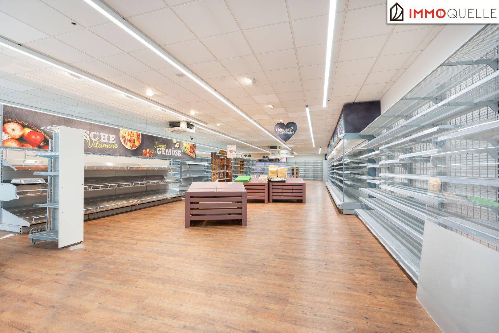 Langer Gang in einem Supermarkt mit leeren Regalen und Holzboden, der auf die Bestückung wartet.