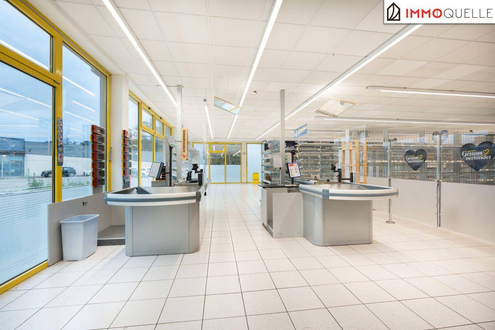 Kassenbereich eines Supermarktes mit mehreren leeren Kassen und großen Fenstern, die Tageslicht hereinlassen.