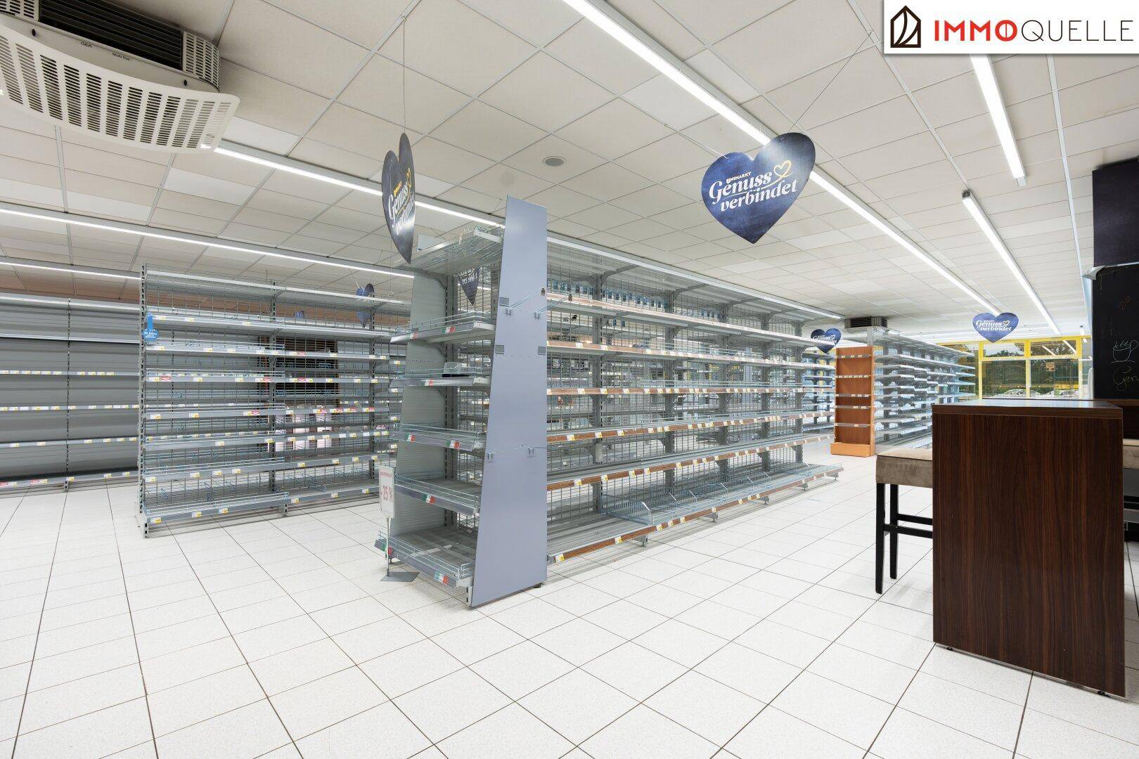 Innenansicht eines Supermarktes mit leeren Regalen und Deckenbeleuchtung, die auf die Einrichtung wartet.