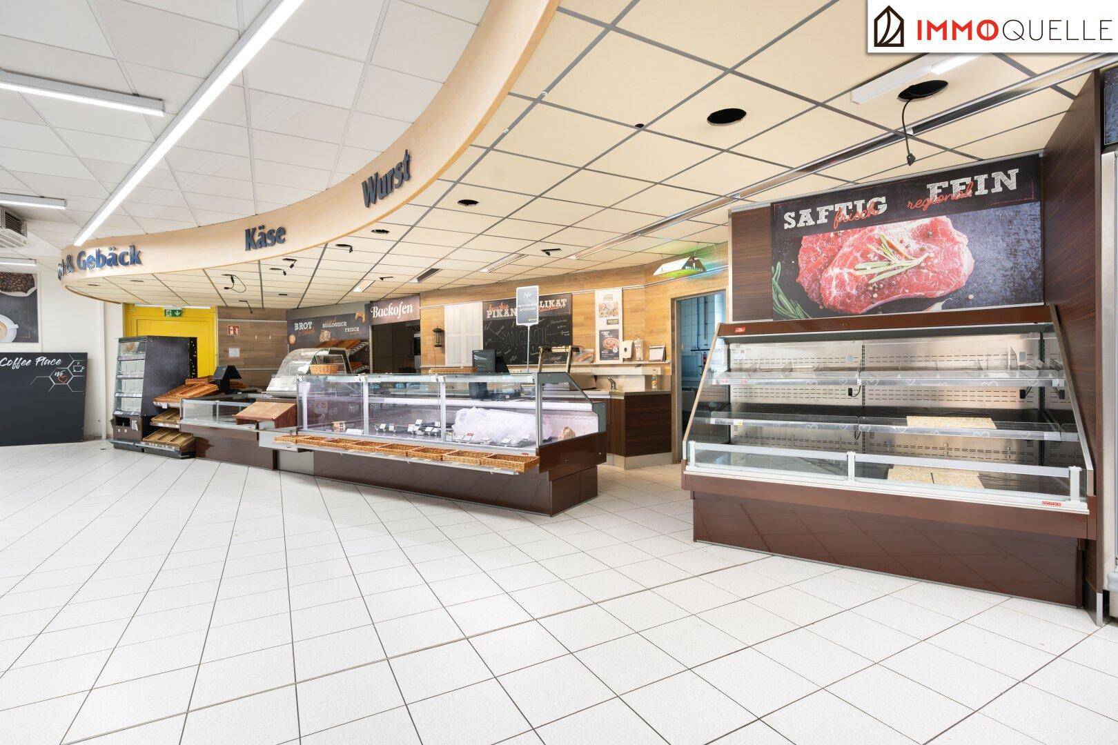 Innenansicht eines Supermarktes mit einer gut beleuchteten Frischetheke für Wurst, Käse und Fleisch.