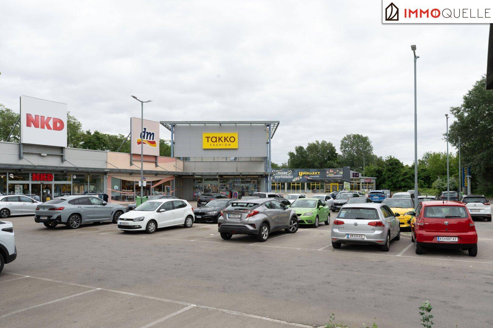 Belebtes Einkaufszentrum mit mehreren Geschäften und einem großen, gut frequentierten Parkplatz.
