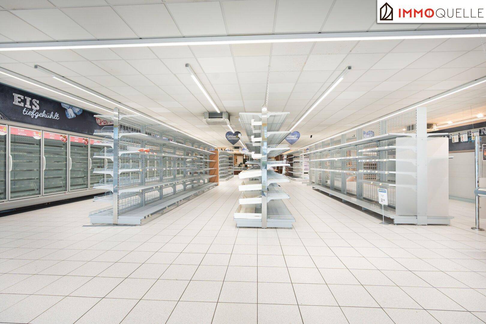 Gangbereich in einem Supermarkt mit leeren Regalen und Gefriertruhen, die auf die Befüllung warten.