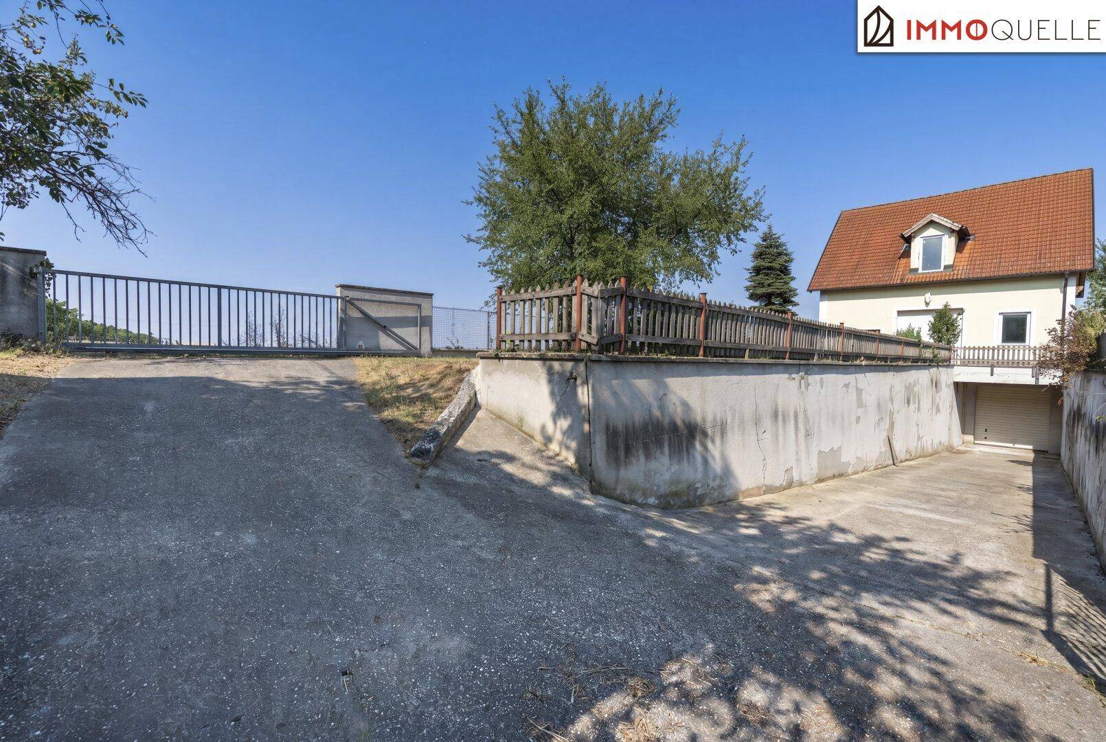 Zufahrt zu einer Tiefgarage mit einem Einfamilienhaus im Hintergrund und einem Metalltor.