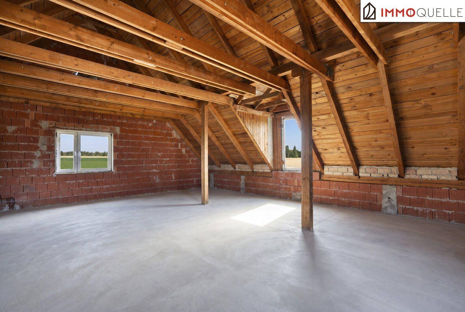 Unausgebauter Dachboden mit sichtbaren Holzbalken, Ziegelwänden und Betonboden, bereit zum Ausbau.