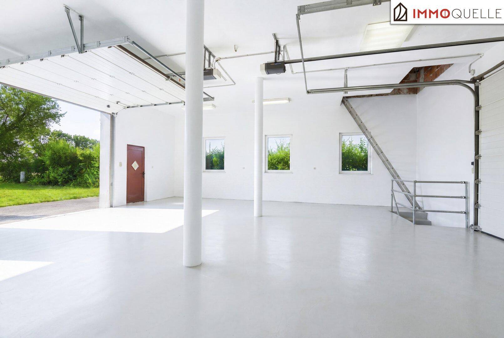 Geräumige, helle Halle mit hohen Decken, großen Garagentoren und mehreren Fenstern.