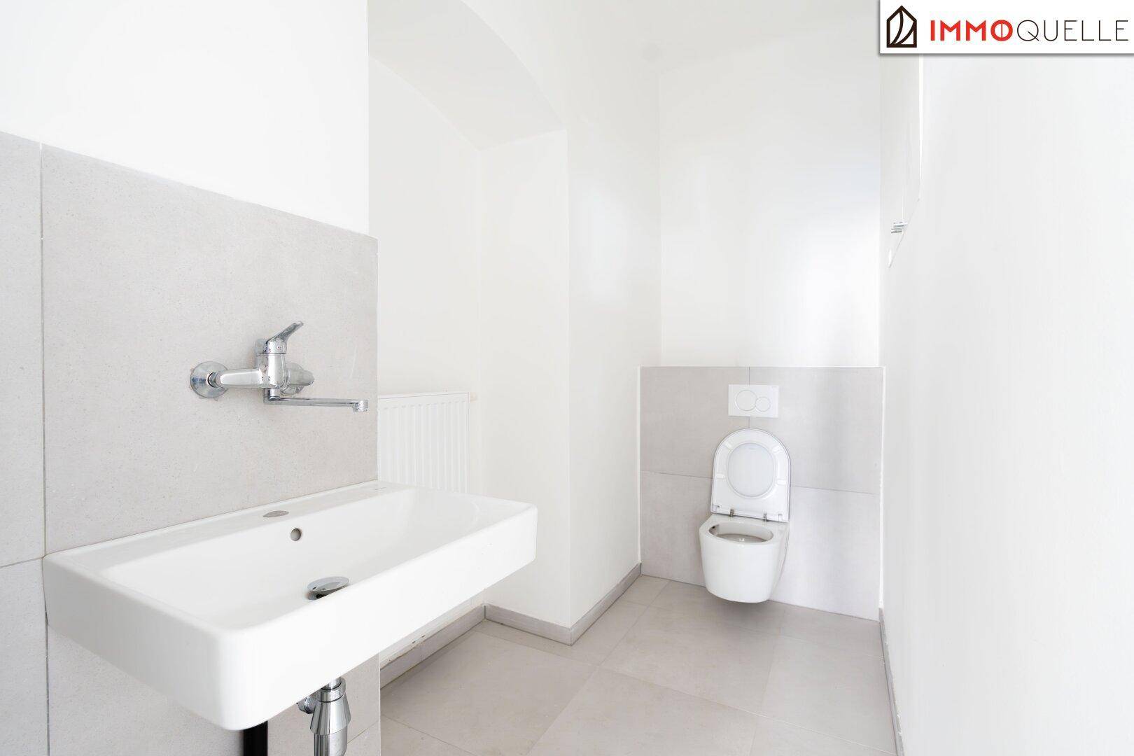 Modernes WC mit wandhängender Toilette, Waschbecken und hellen Fliesen an Wänden und Boden.