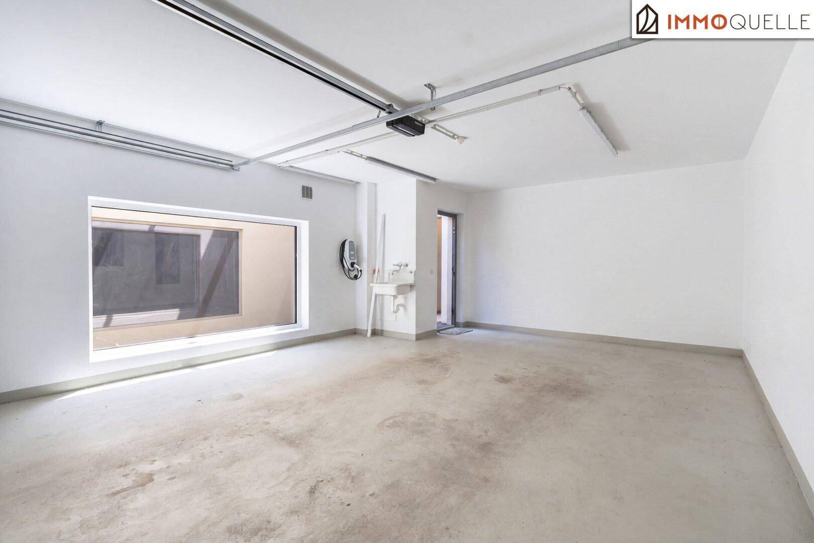 Geräumige Garage mit Betonboden, großem Fenster und Zugang zum Innenbereich des Hauses.
