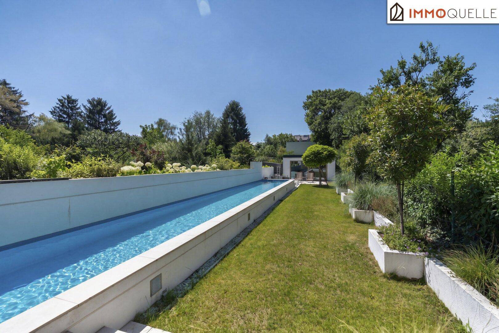 Langer, schmaler Pool umgeben von Rasenflächen und grüner Bepflanzung in sonniger Umgebung.