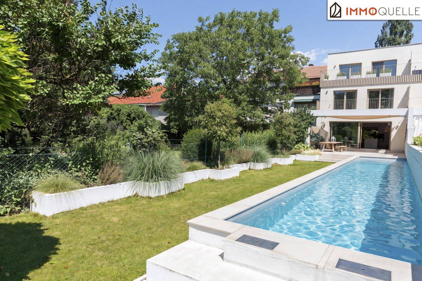 Gepflegter Garten mit langem Pool und üppiger Bepflanzung unter strahlend blauem Himmel.