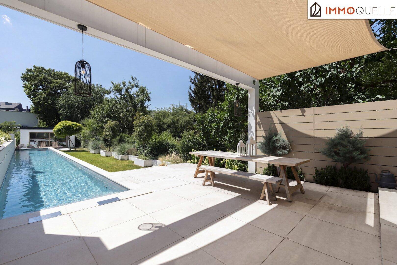 Überdachte Terrasse mit Holztisch und Bänken neben dem langen Swimmingpool im Garten.