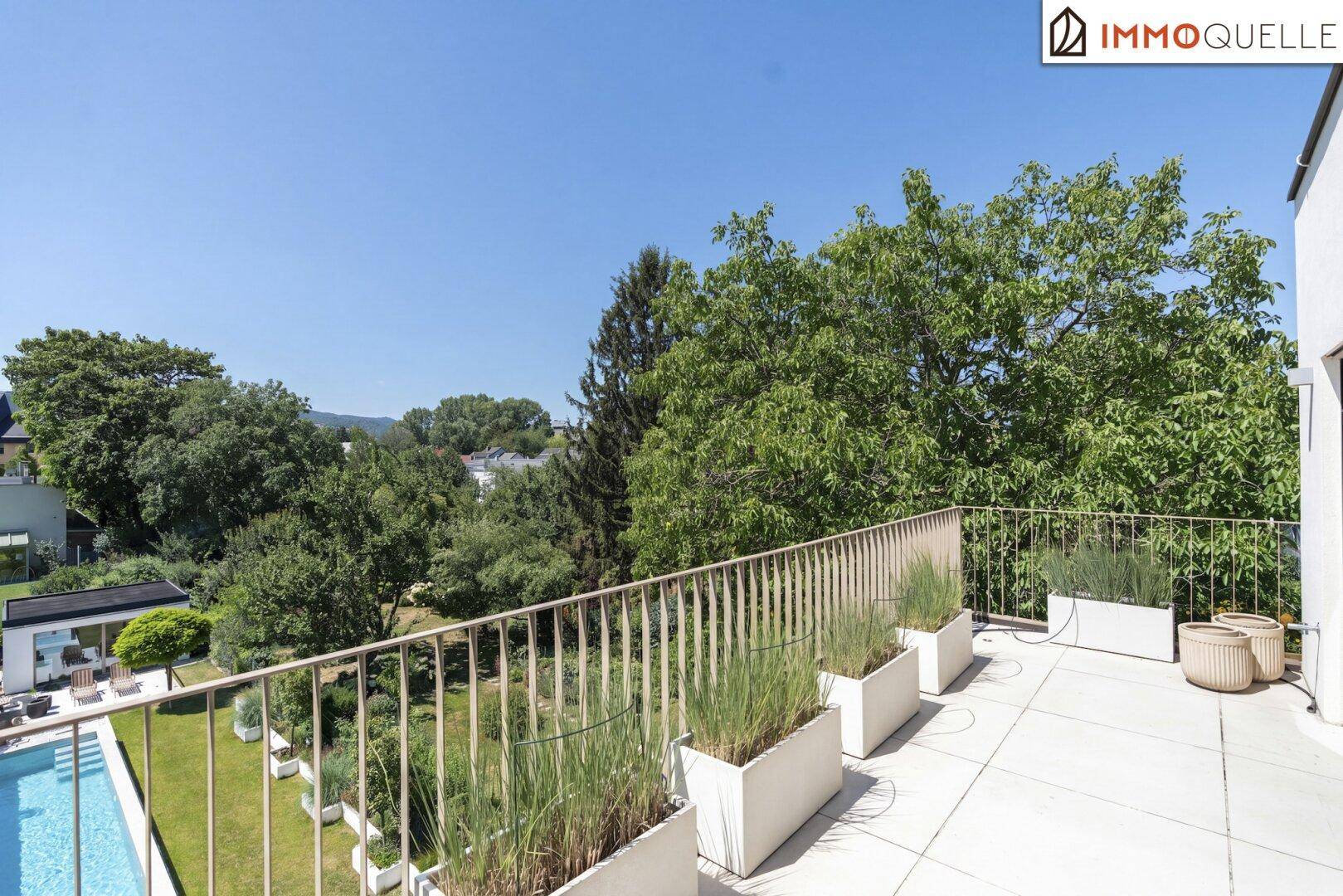 Geräumiger Balkon mit Pflanzenkübeln und weitem Blick auf den Garten und den Poolbereich.