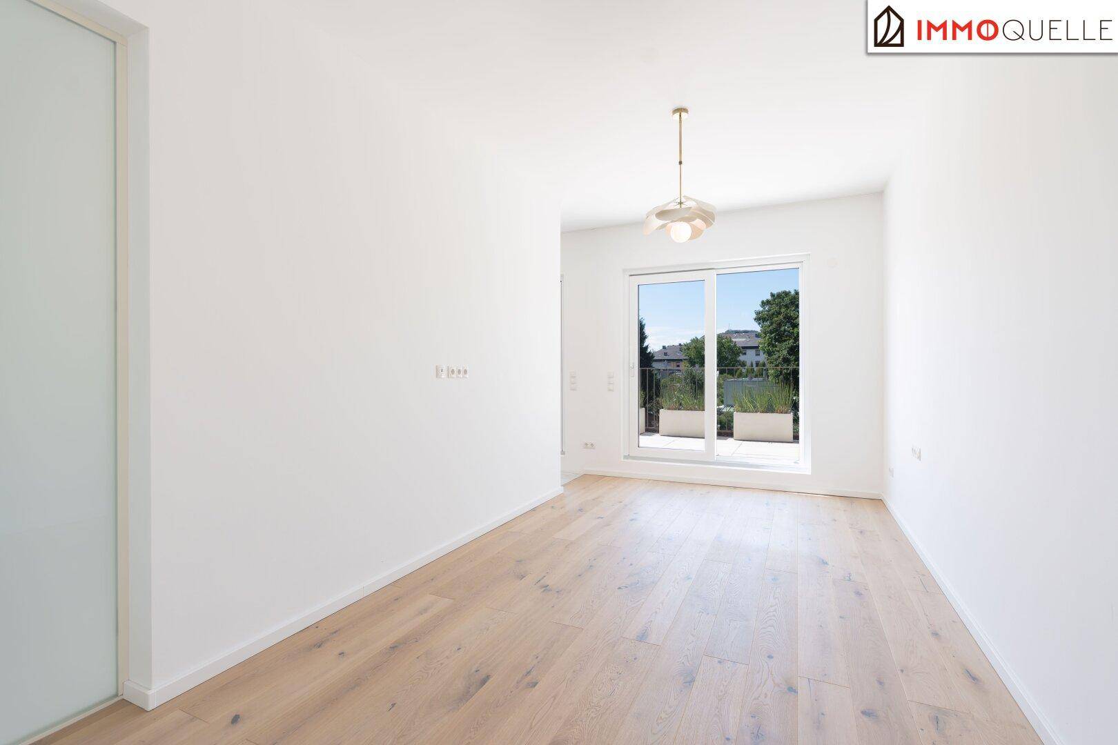 Heller, leerer Raum mit Holzboden und großen Fenstern, die viel Tageslicht hereinlassen.