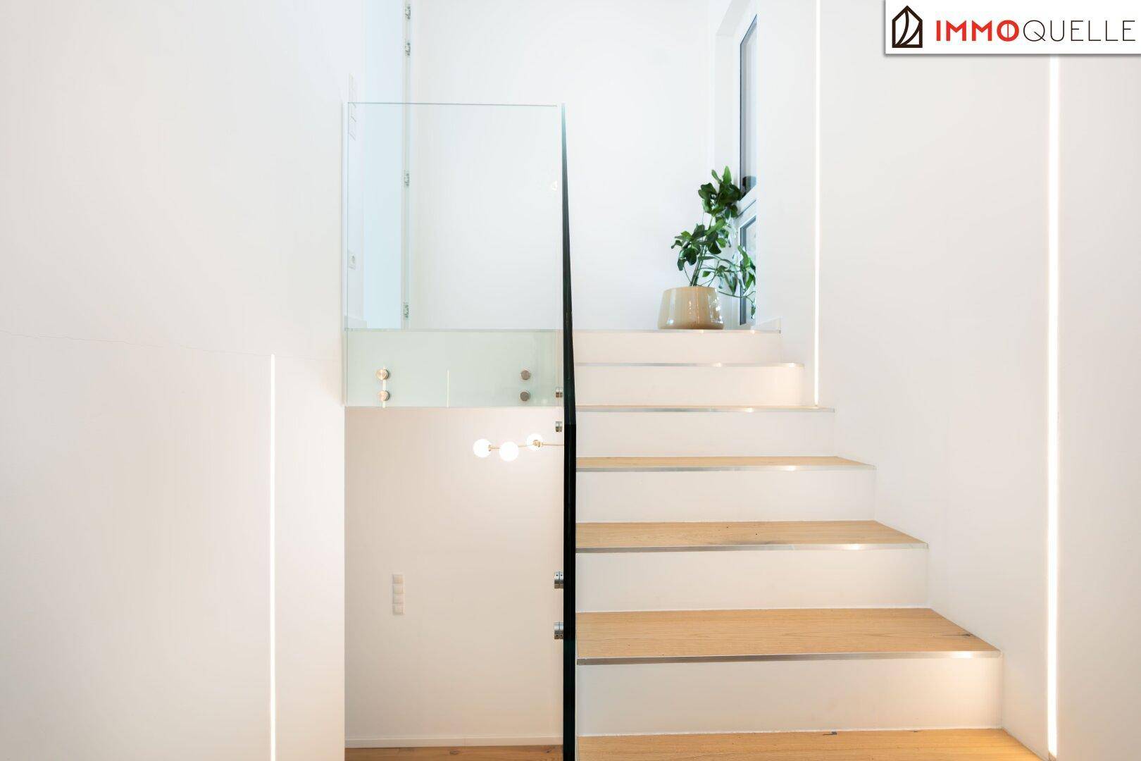 Helles Treppenhaus mit modernen Holzstufen, Glasgeländer und minimalistischer Beleuchtung.