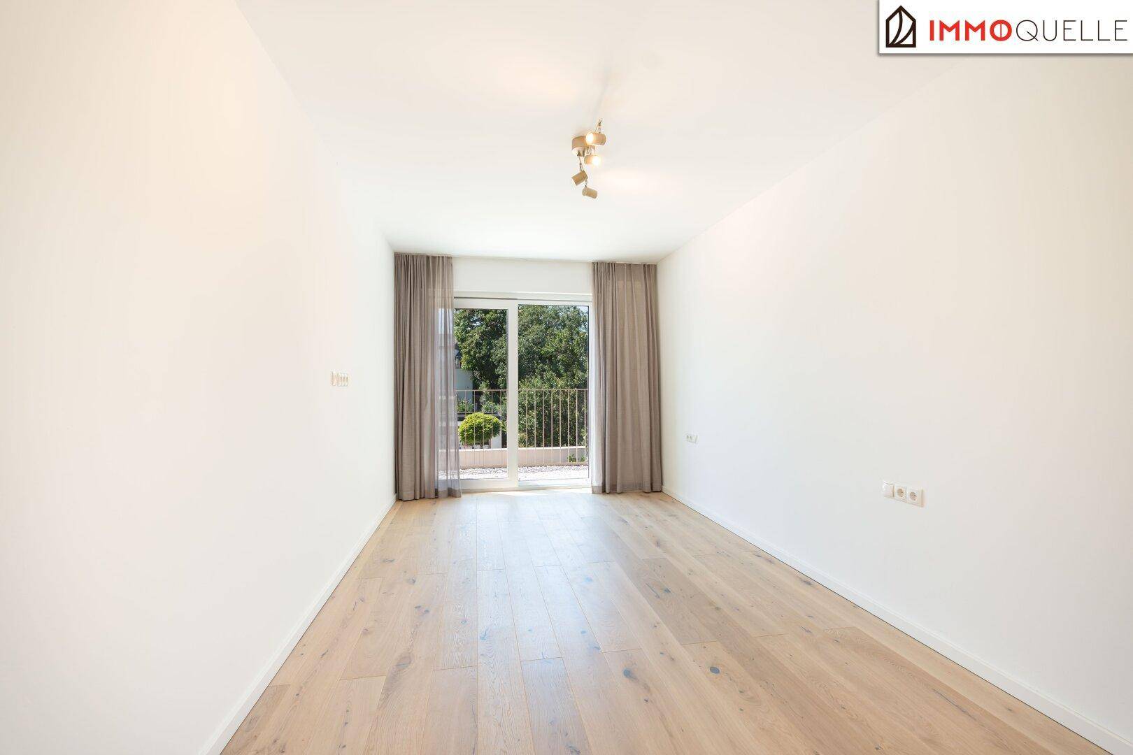 Leerer Raum mit Holzboden und großen Fenstern, die viel natürliches Licht hereinlassen.