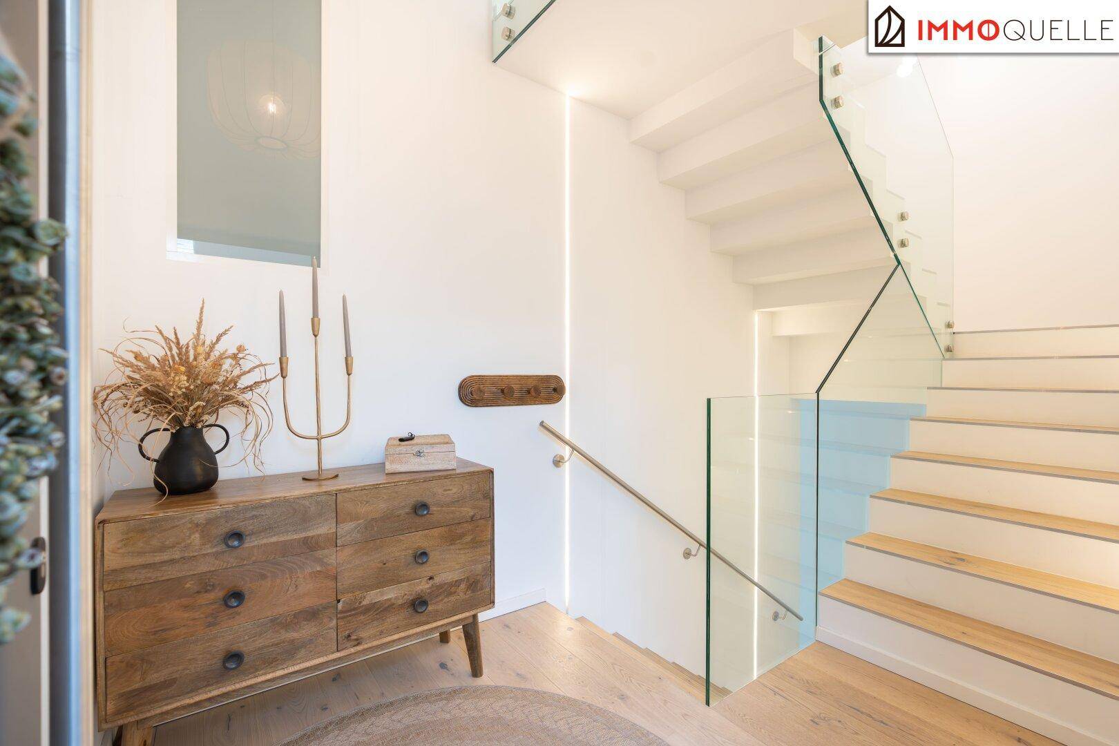 Elegantes Treppenhaus mit Glasgeländer, Holzstufen und indirekter Beleuchtung.