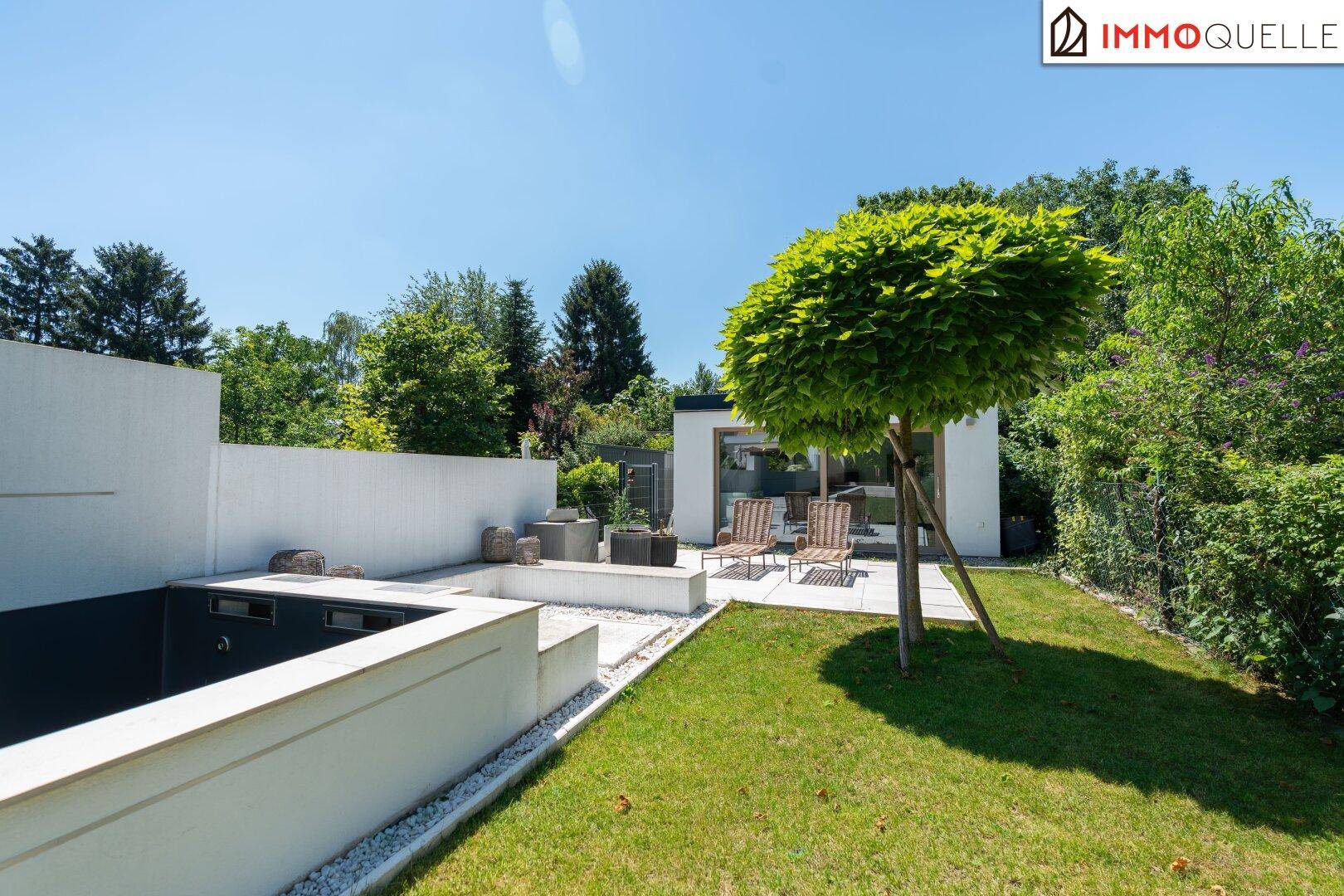 Kleines Gartenhaus mit Terrasse und Liegestühlen, umgeben von Grünflächen und Bäumen.