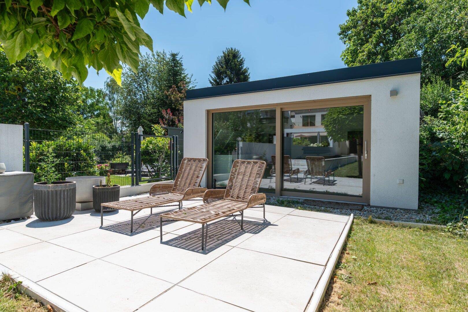 Entspannungsbereich mit Liegestühlen auf der Terrasse und Blick auf das moderne Gartenhaus.