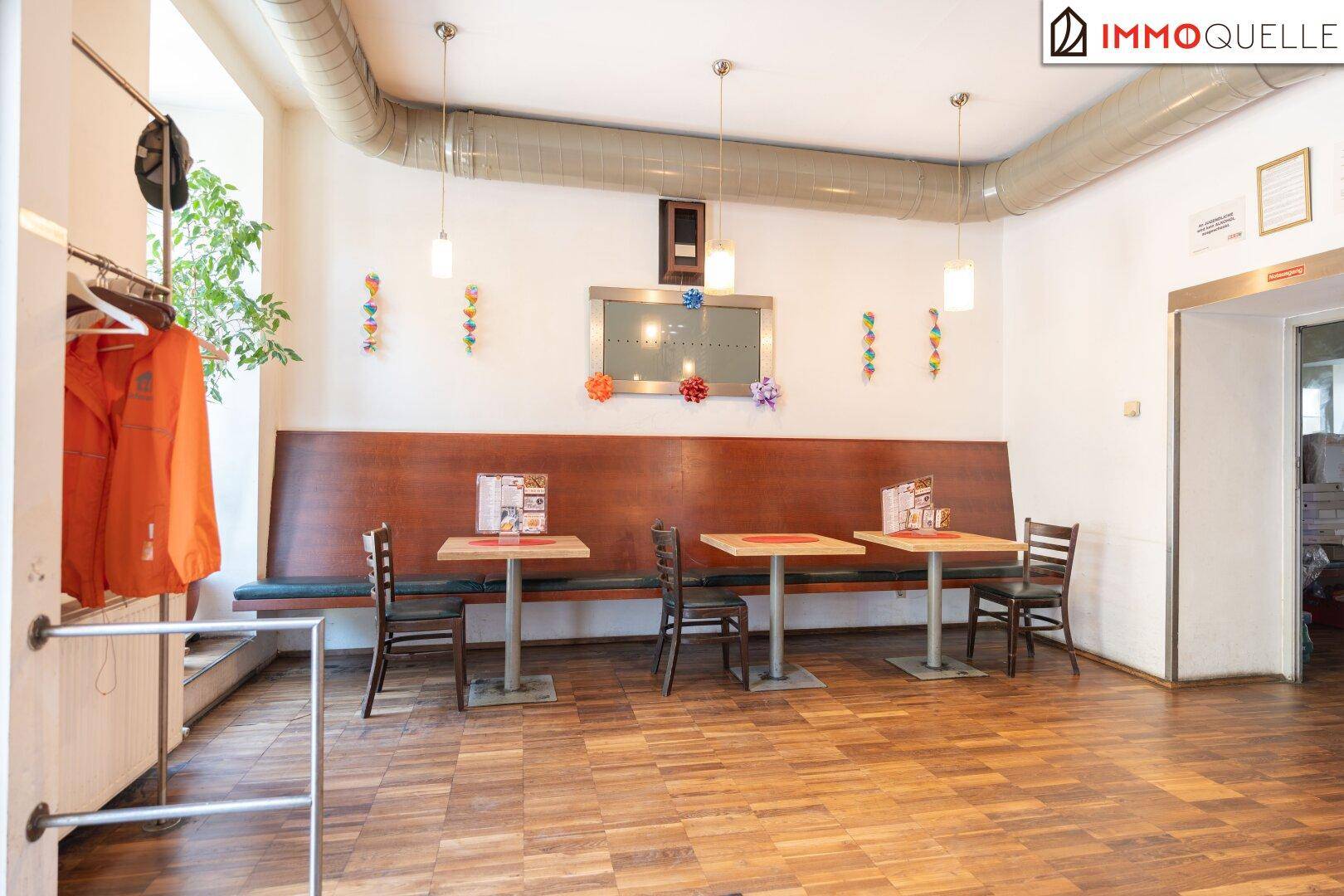 Gemütlicher Restaurantbereich mit Holztischen, Stühlen und einer langen Sitzbank entlang der Wand.