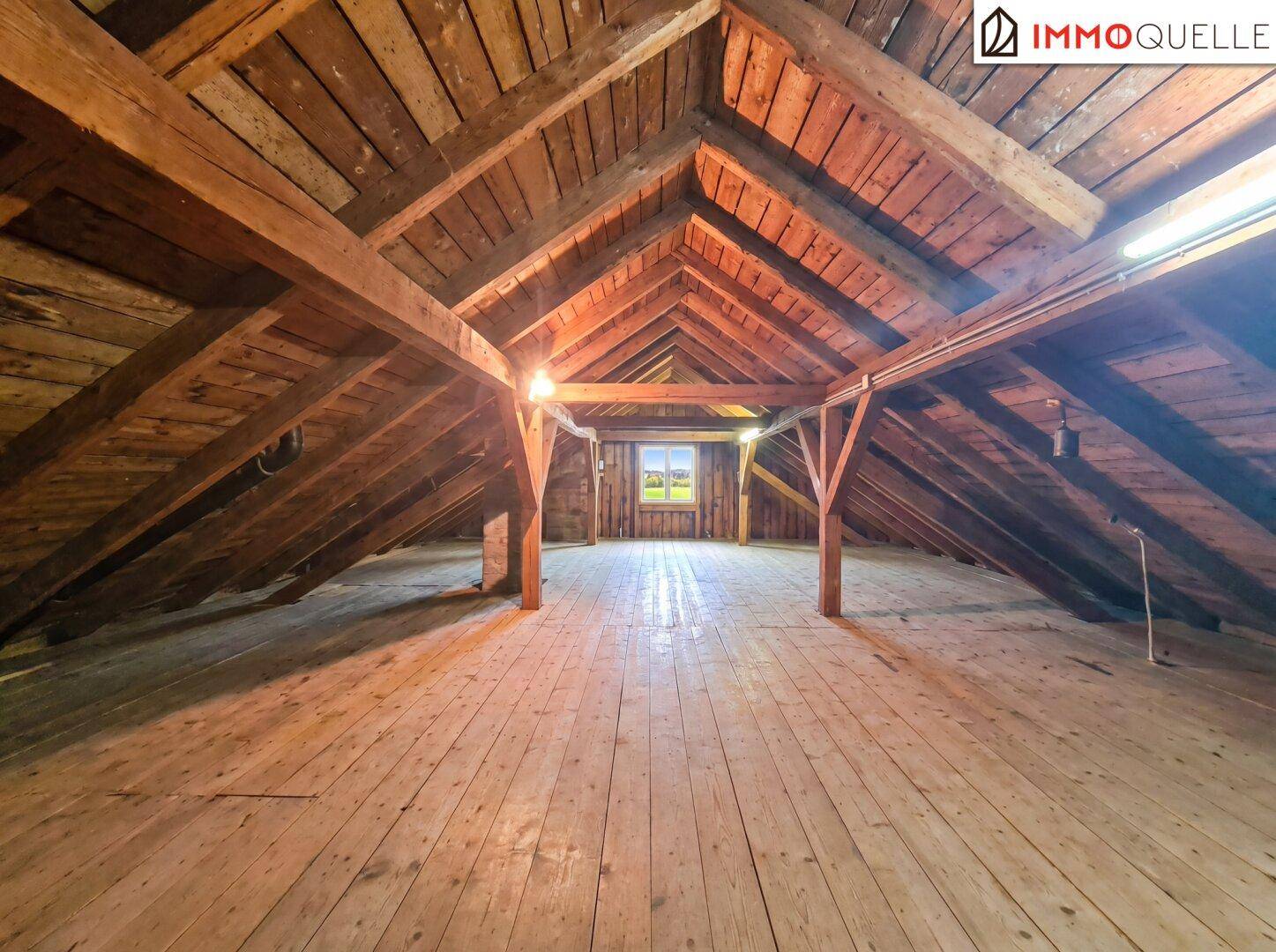 Unausgebauter Dachboden mit sichtbaren Holzbalken und Holzdielenboden.