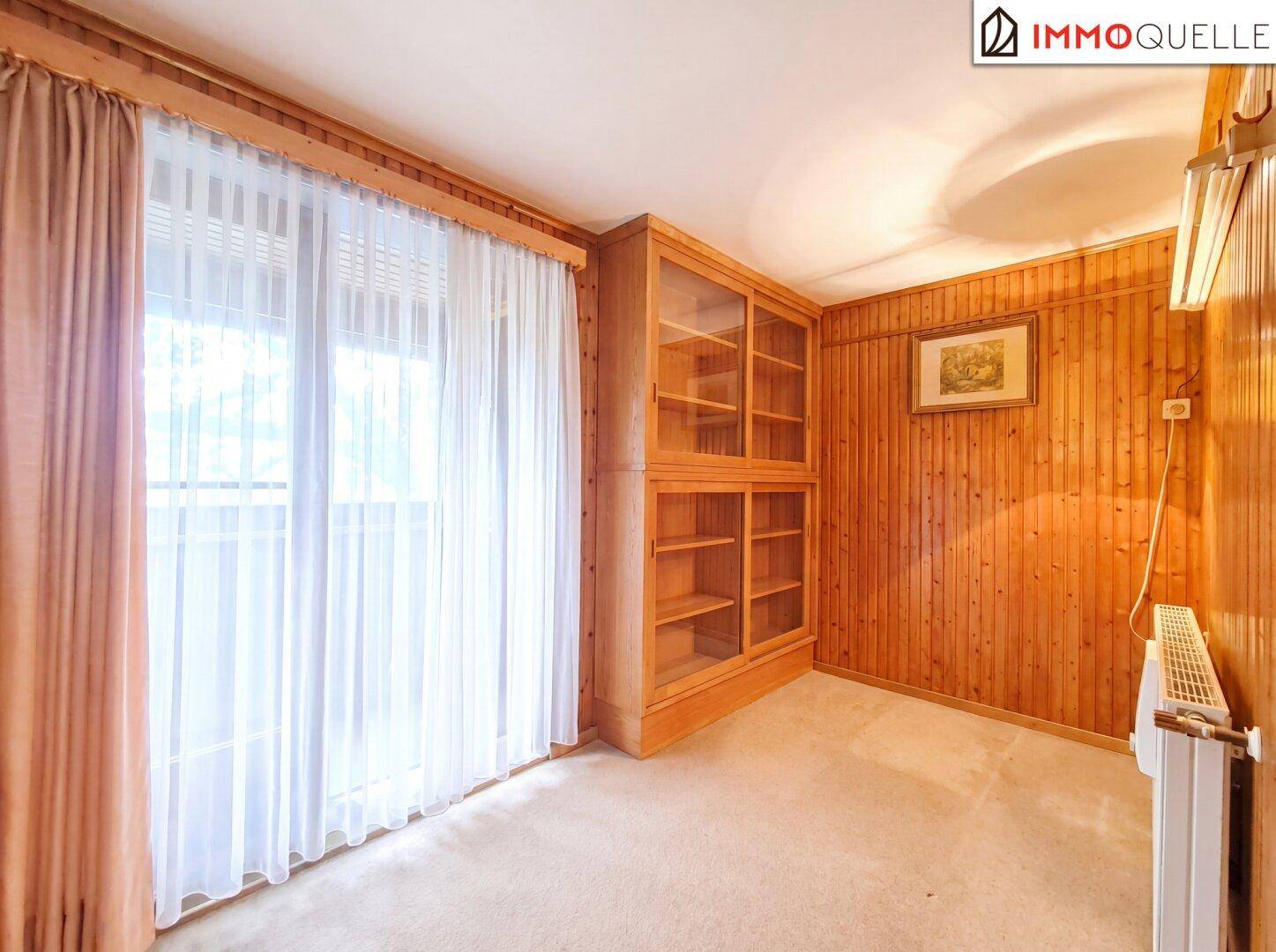 Arbeitszimmer mit Holzvertäfelung, Einbauschränken und großem Fenster.