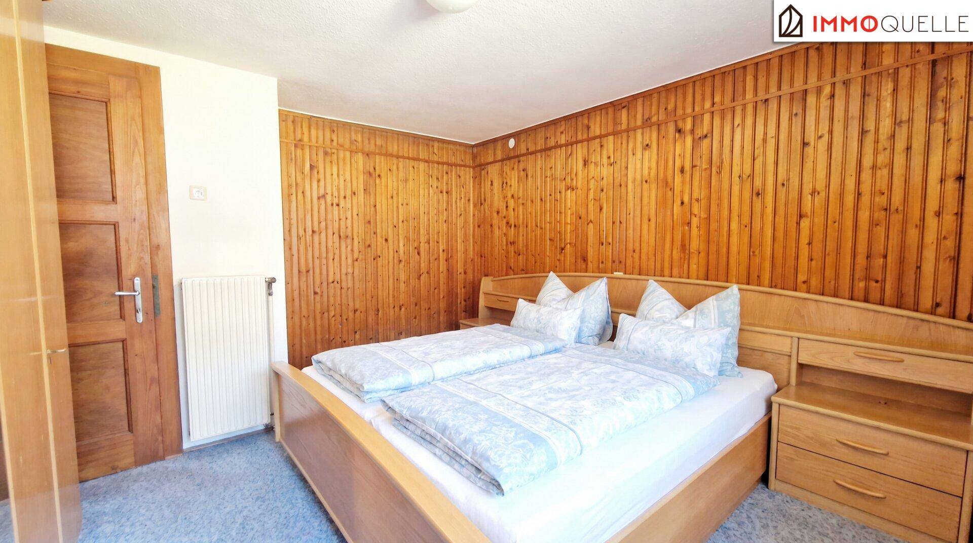 Schlafzimmer mit Holzvertäfelung, Doppelbett und Teppichboden.