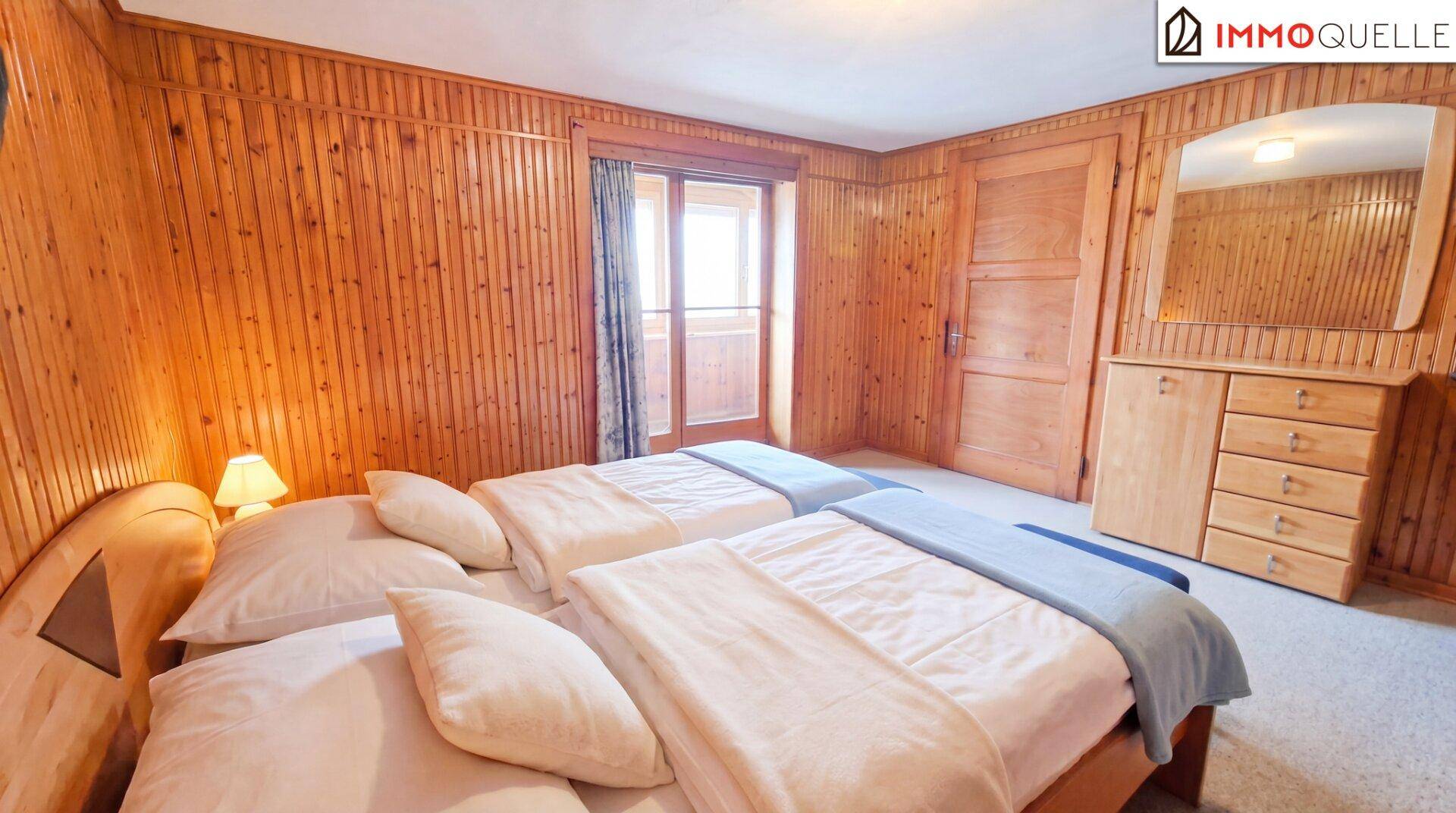 Schlafzimmer mit Holzvertäfelung, zwei Einzelbetten und Zugang zu einem Balkon.