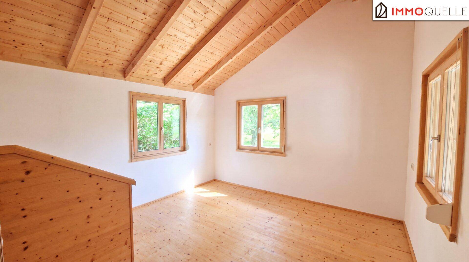 Helles Zimmer im Dachgeschoss mit Holzboden, Holzdecke und Fenstern.
