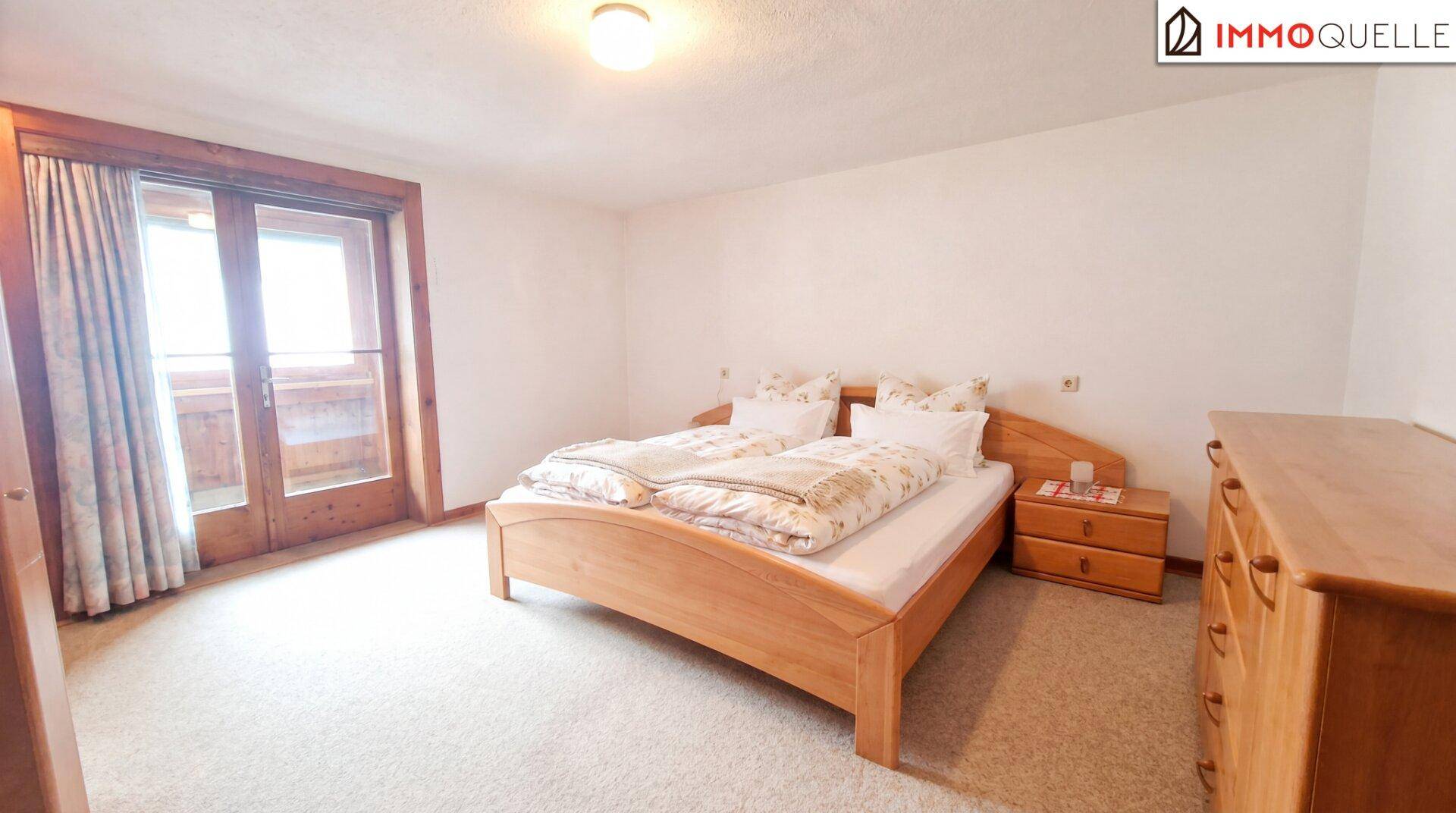 Schlafzimmer mit Doppelbett, Teppichboden und Zugang zu einem Balkon.