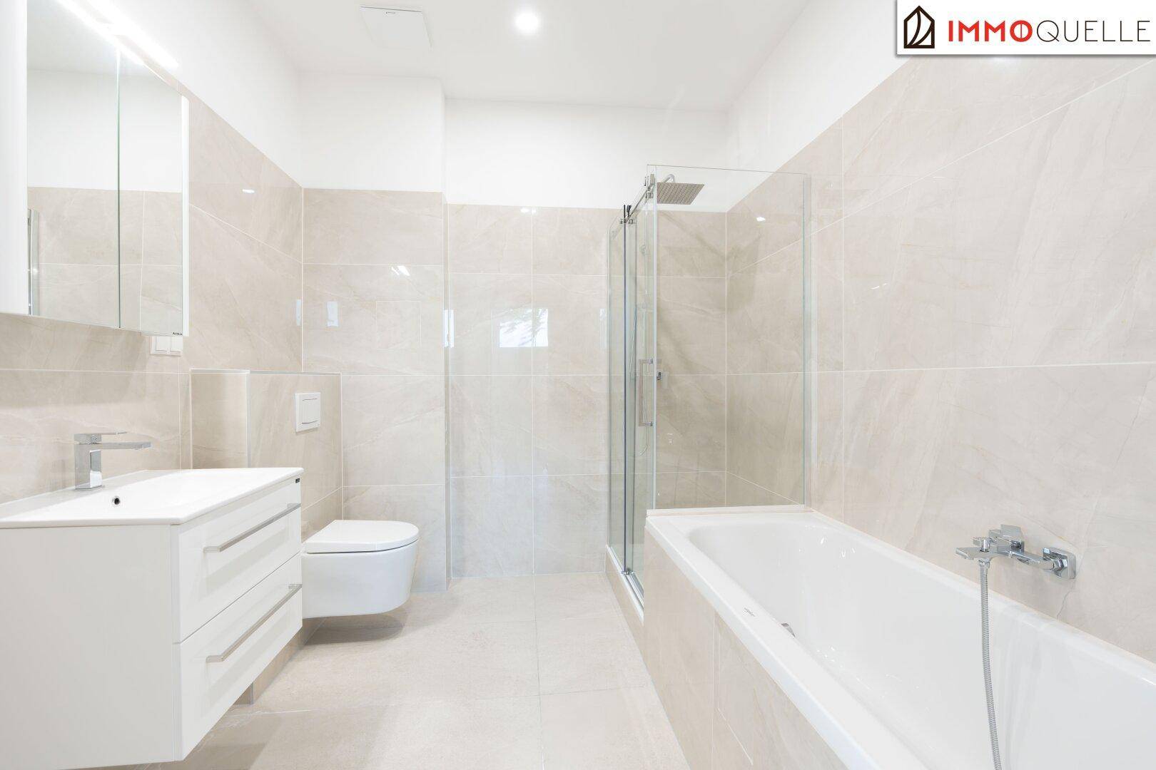 Modernes Badezimmer mit hellen Fliesen, Waschtisch, wandhängendem WC und Badewanne mit Duschabtrennung.