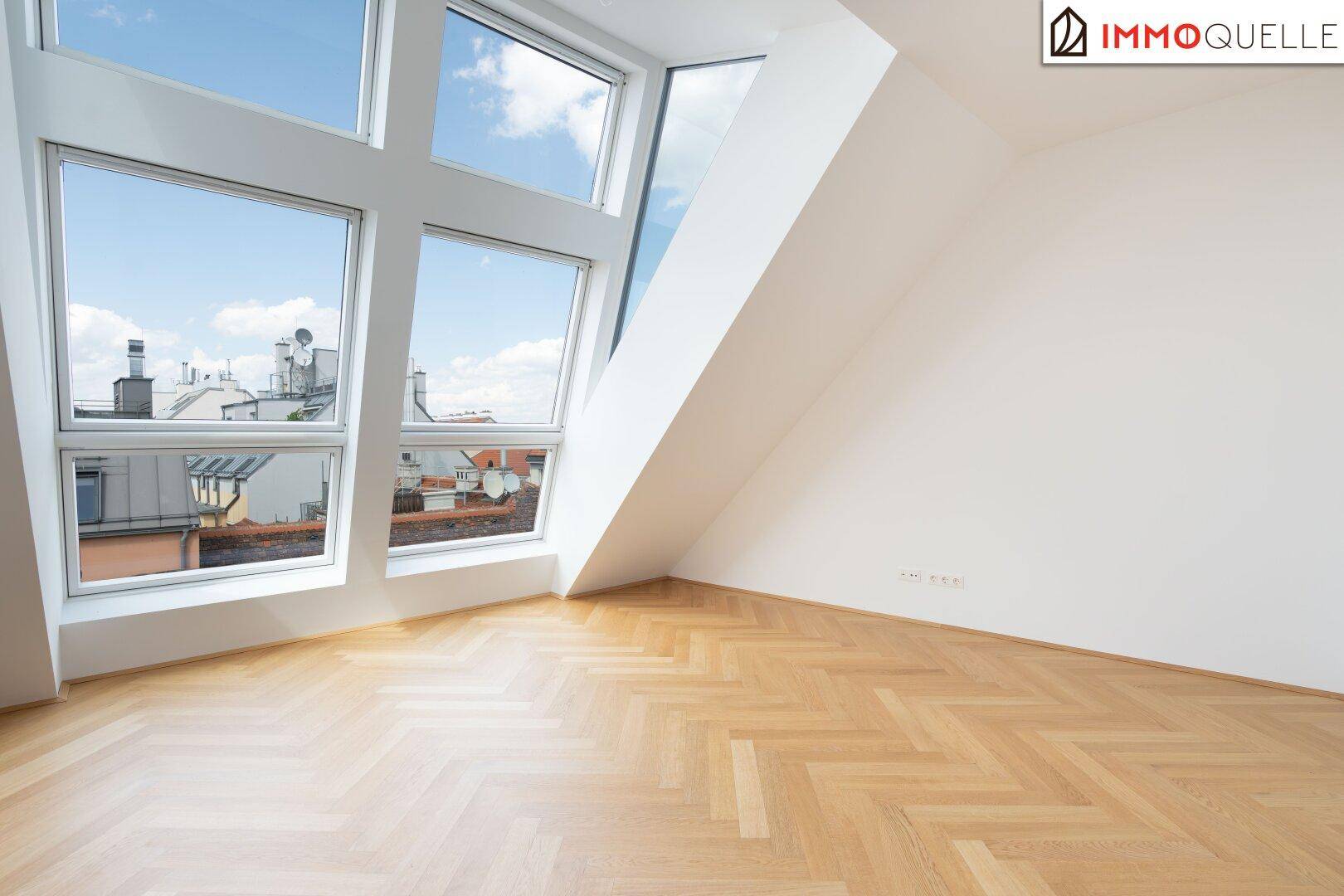 Leeres Schlafzimmer mit Holzboden, Dachschrägen und großer Fensterfront für viel Licht.