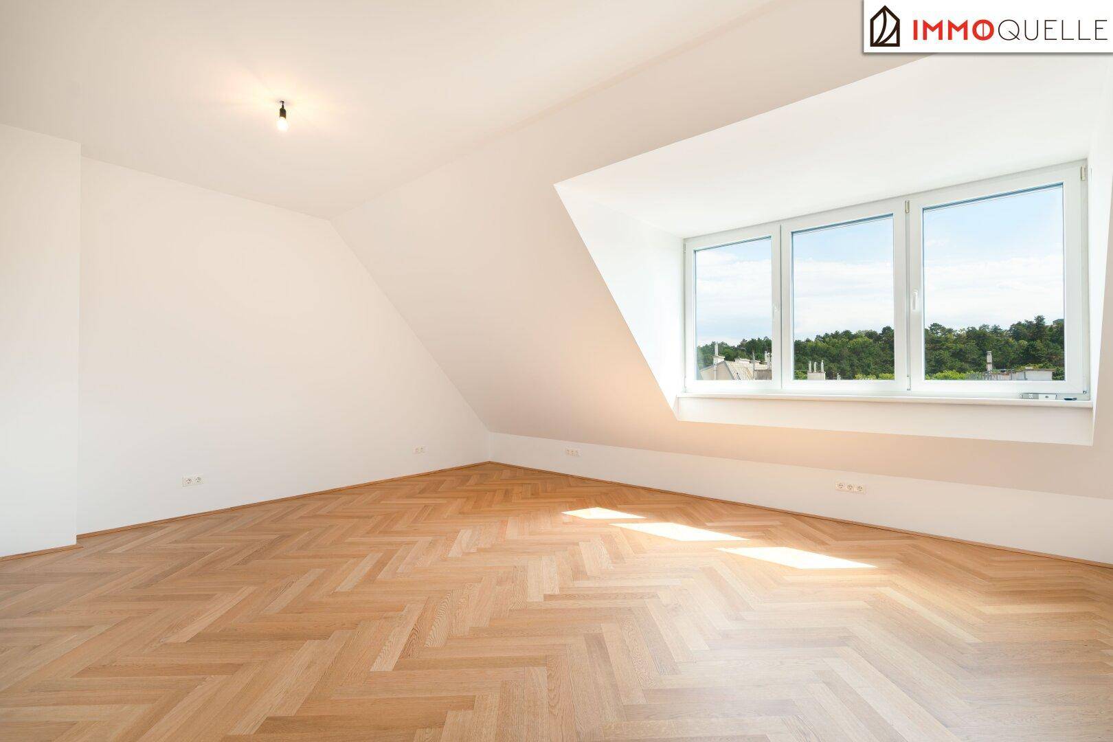 Leeres Schlafzimmer mit Holzboden, Dachschrägen und breitem Fenster mit Grünblick.
