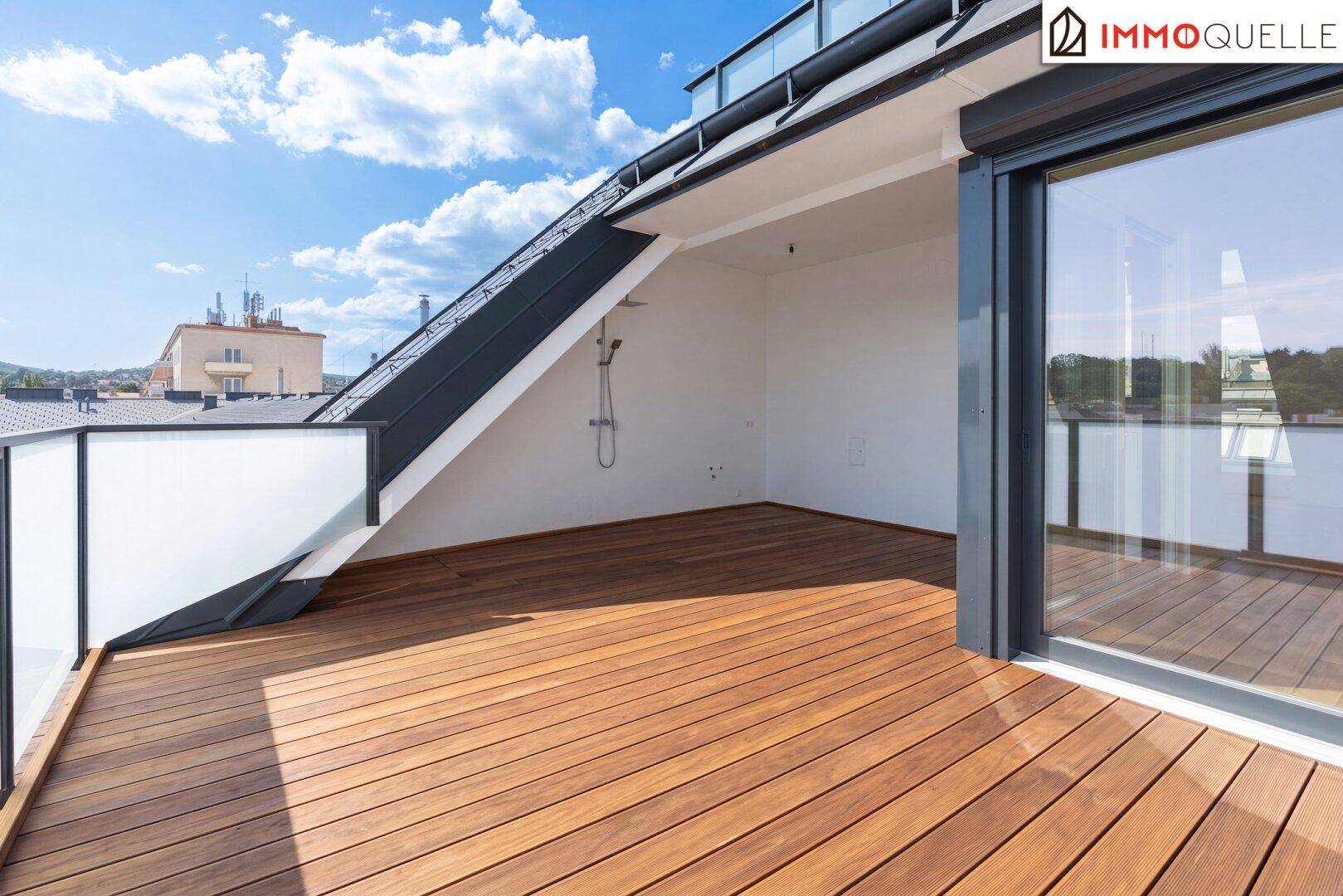 Geräumige Dachterrasse mit Holzbelag, Außendusche und Blick über die Stadt.