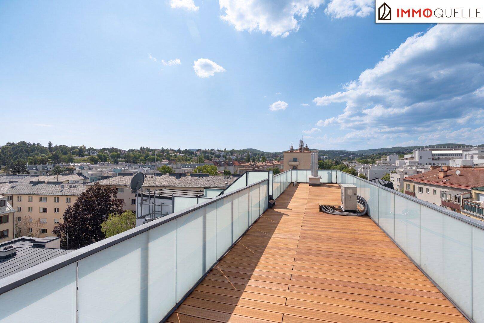 Weitläufige Dachterrasse mit Holzbelag und weitem Blick über die Stadt und grüne Hügel.