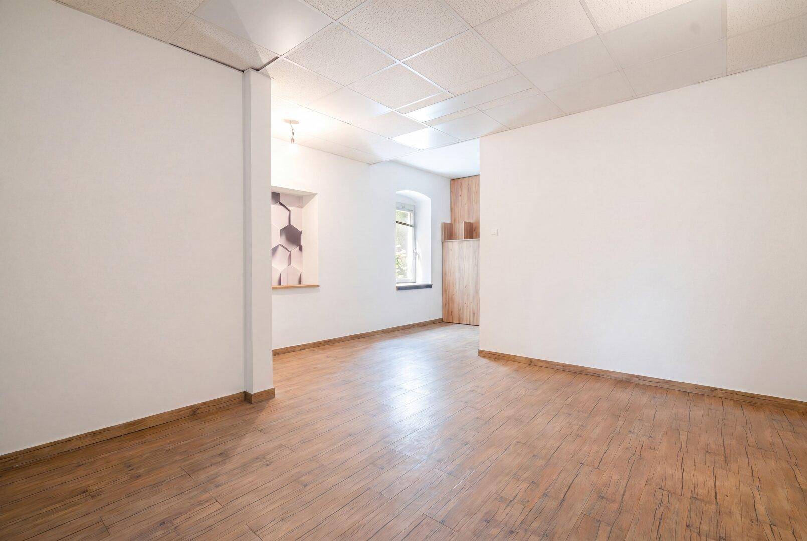 Kleinerer Büroraum mit Holzoptikboden, weiß gestrichenen Wänden und einem Fenster.
