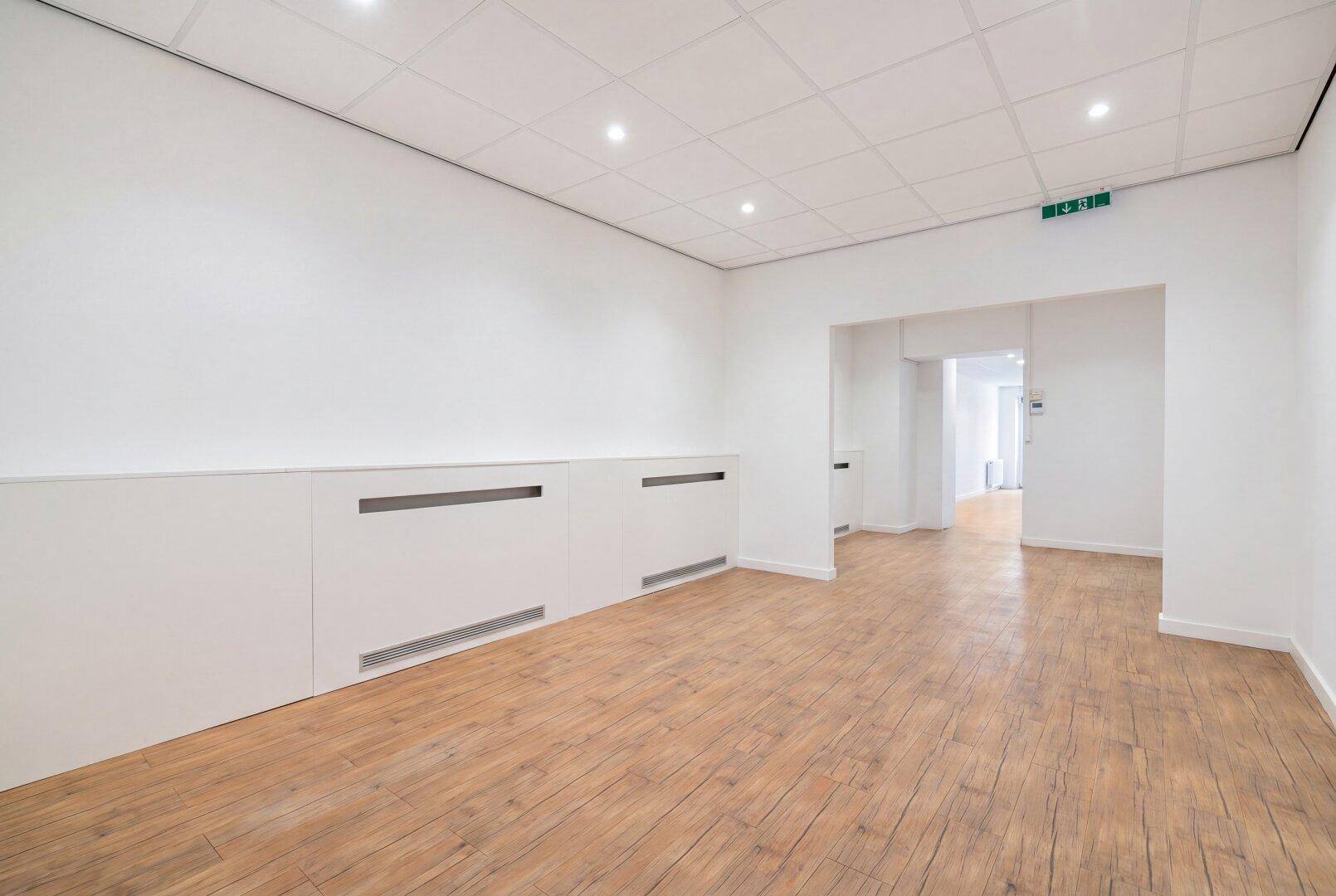 Heller Büroraum mit Holzoptikboden, abgehängter Decke und integrierten Wandpaneelen.